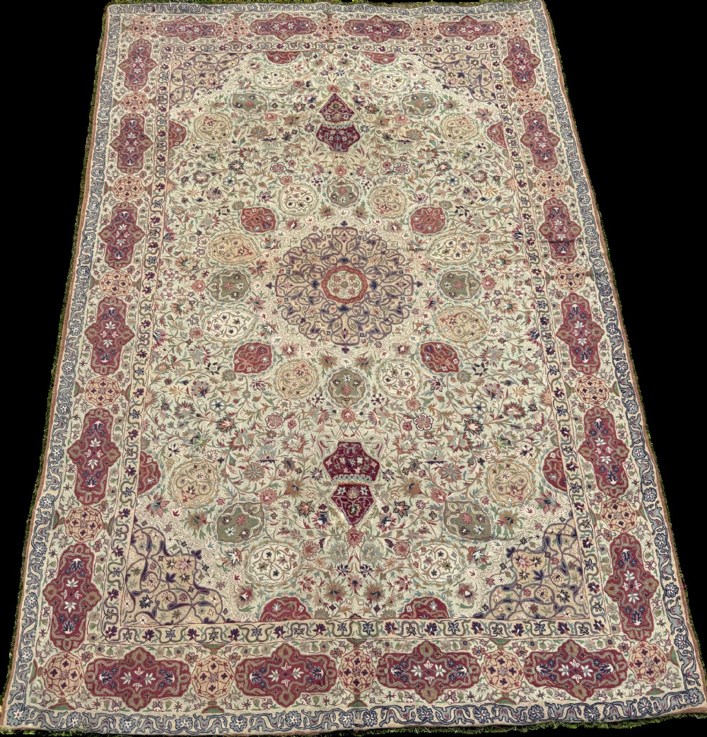 A rectangular hand-embroidered crewelwork carpet featuring a central medallion and intricate floral motifs in burgundy, green, and navy blue on a cream ground. View VI