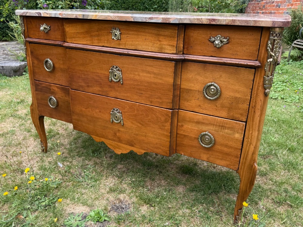 A French Transitional style cherrywood commode featuring a contoured marble top, decorative brass mounts, and cabriole legs.