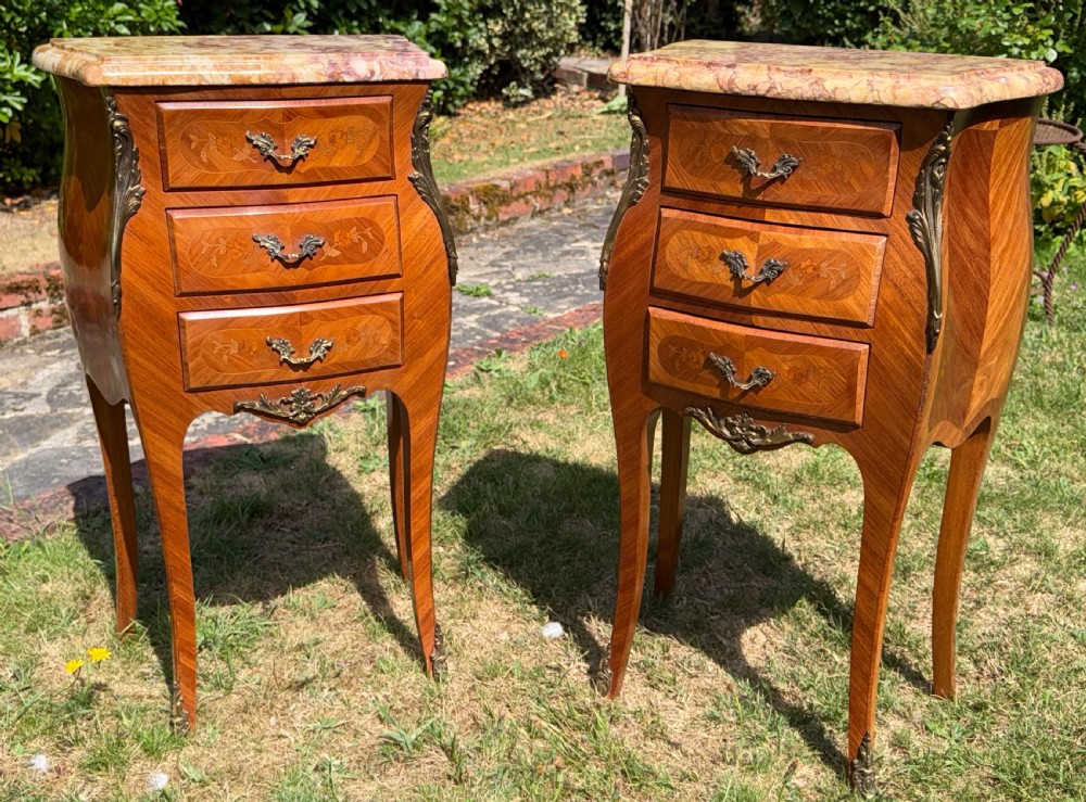 A pair of French Louis XV style marquetry bedside tables featuring marble tops, three floral inlaid drawers, gilt bronze mounts, and slender cabriole legs.