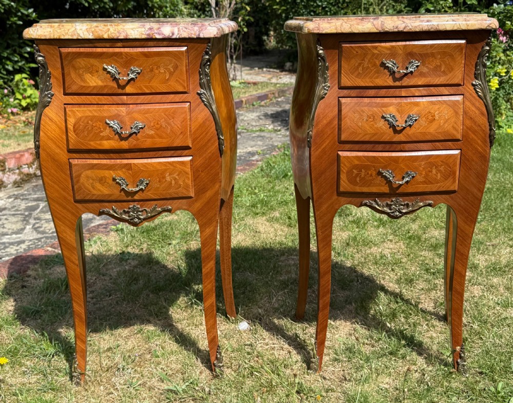 A pair of French Louis XV style marquetry bedside tables featuring marble tops, three floral inlaid drawers, gilt bronze mounts, and slender cabriole legs. View V