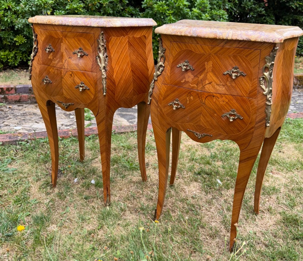Pair of French Rococo style bedside tables featuring floral wood marquetry, curved cabriole legs, gilt metal mounts, and polished marble tops.