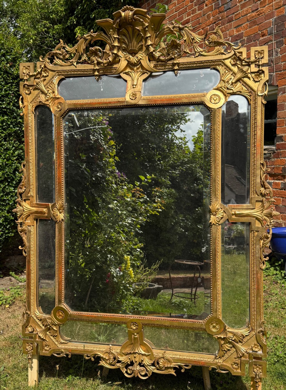 An ornate nineteenth-century French giltwood cushion mirror featuring a central bevelled plate surrounded by border glass panels and elaborate scrollwork cresting.