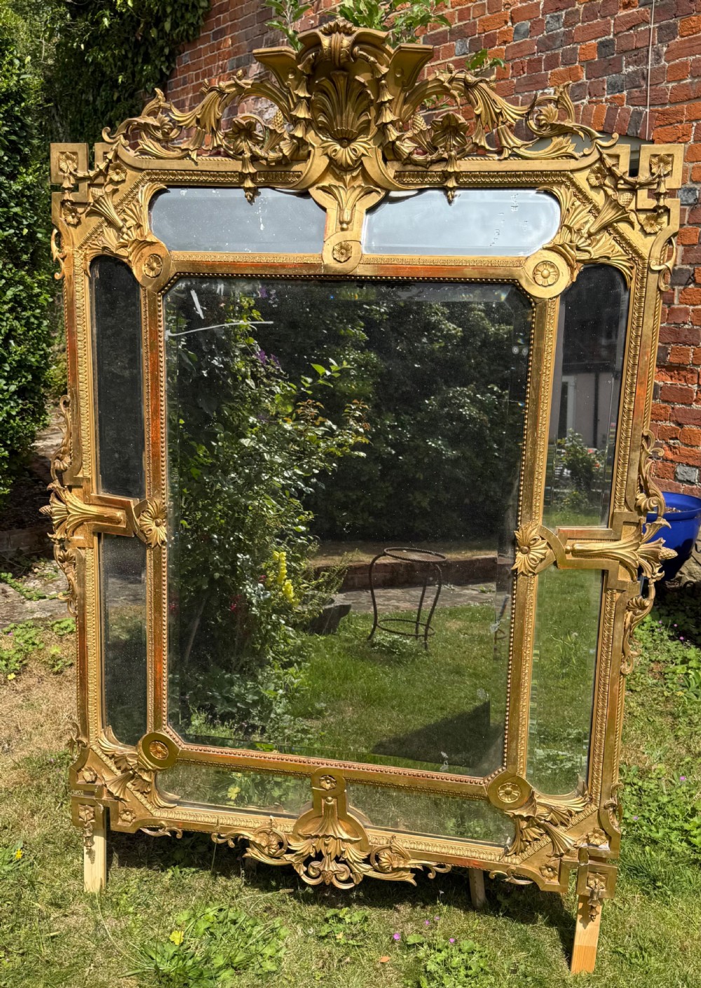 An ornate nineteenth-century French giltwood cushion mirror featuring a central bevelled plate surrounded by border glass panels and elaborate scrollwork cresting. View II