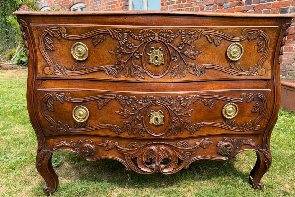 An 18th-century French Provencal walnut commode featuring a serpentine front, intricate ribbon and foliage carvings, two drawers with brass ring handles, and cabriole legs. View III