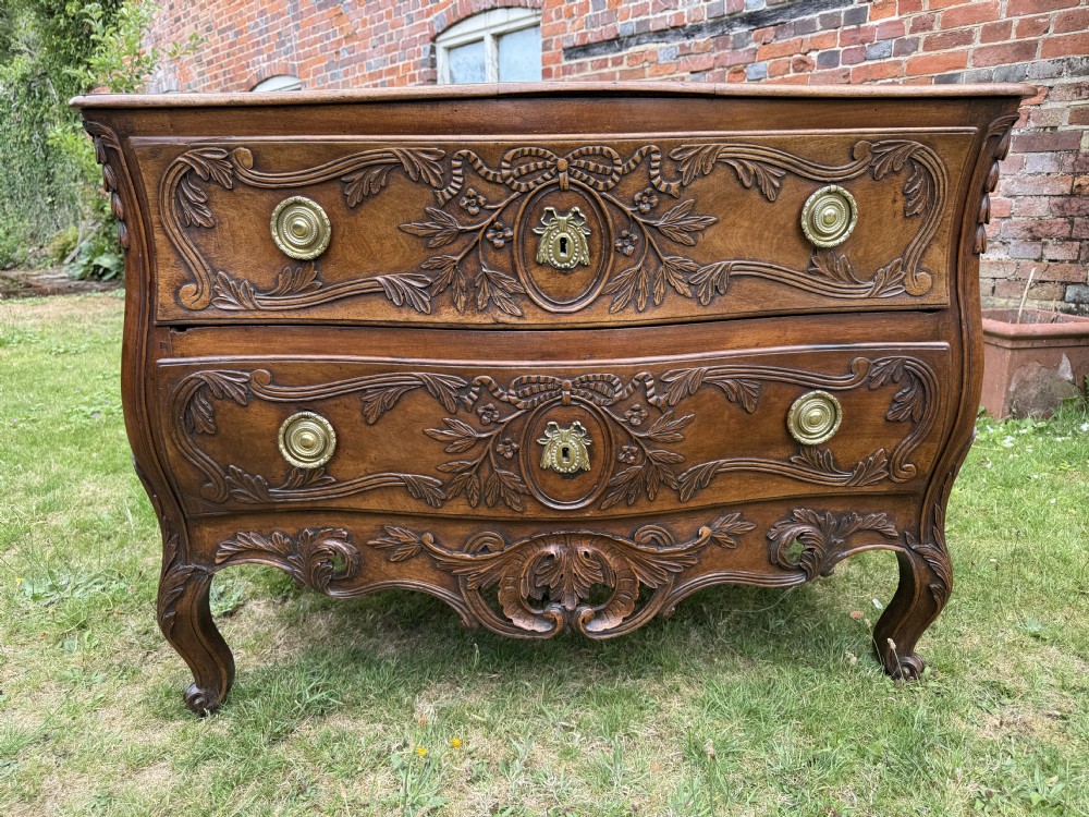 An 18th-century French Provencal walnut commode featuring a serpentine front, intricate ribbon and foliage carvings, two drawers with brass ring handles, and cabriole legs. View II