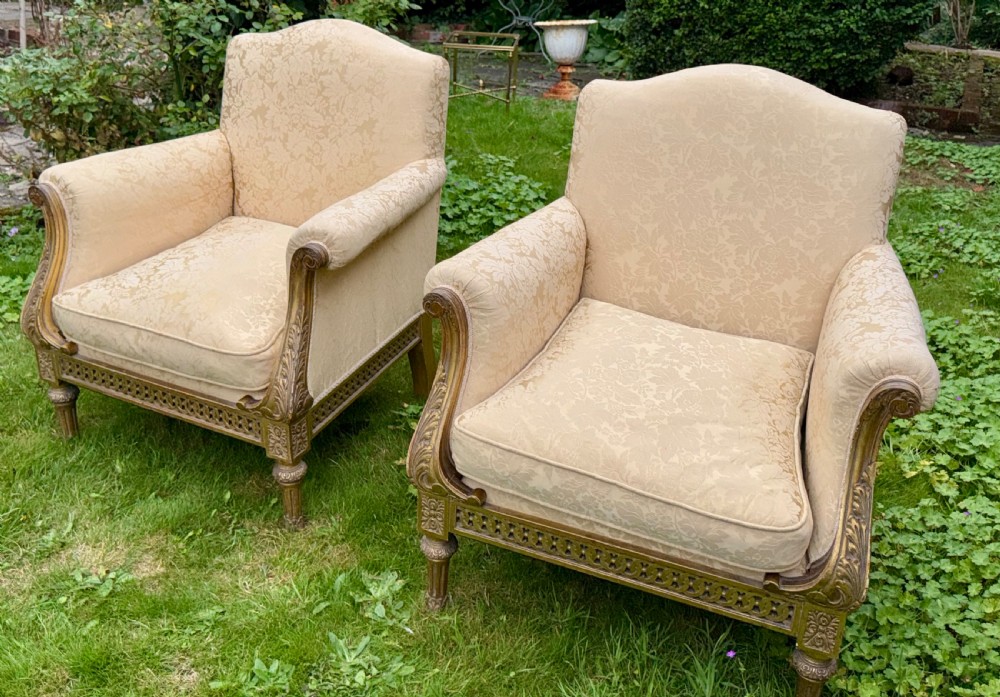 A pair of giltwood armchairs upholstered in cream damask pattern fabric with matching footstools. View II