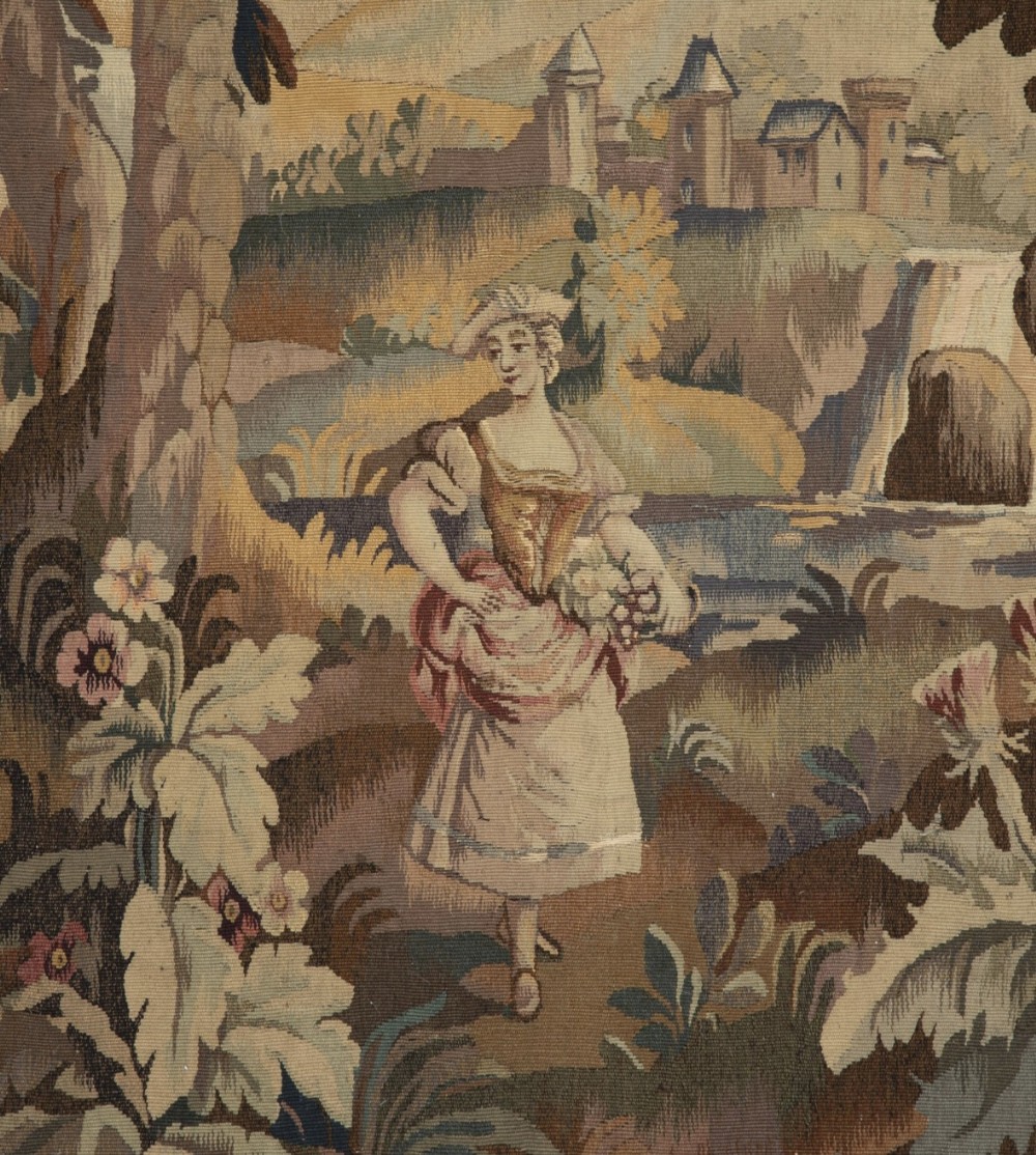 An early nineteenth-century French Aubusson wall tapestry depicting a female figure carrying a flower basket within a pastoral landscape featuring trees, foliage, and architectural towers.