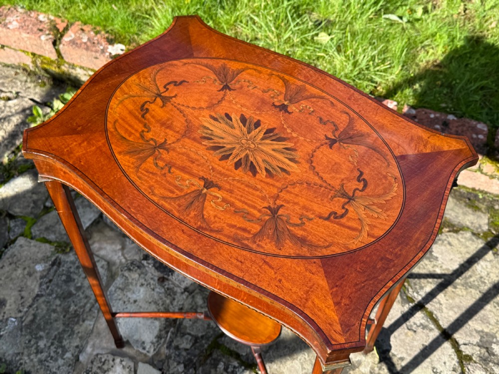 An Edwardian mahogany occasional table featuring a shaped top decorated with a central oval marquetry motif, slender tapered legs, and an X-stretcher with an oval centre platform. View II