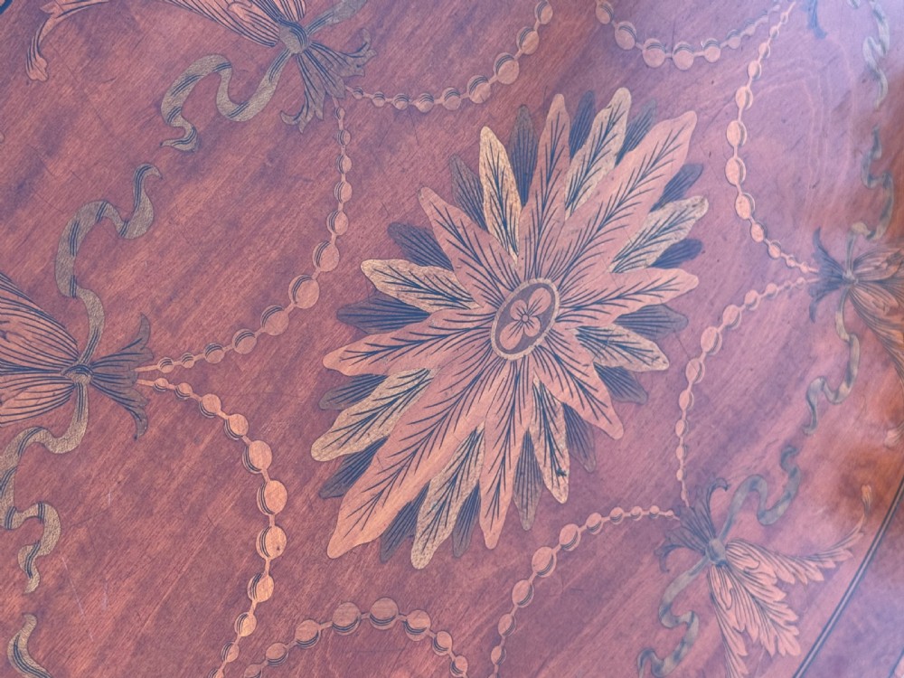 An Edwardian mahogany occasional table featuring a shaped top decorated with a central oval marquetry motif, slender tapered legs, and an X-stretcher with an oval centre platform. View VI