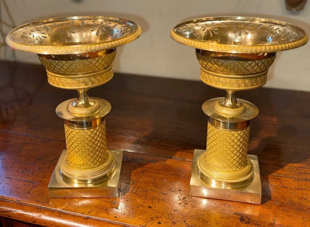 A pair of French Empire gilt bronze tazzas featuring pierced rims, engine-turned lattice patterns, pedestal stems, and square plinth bases. View V