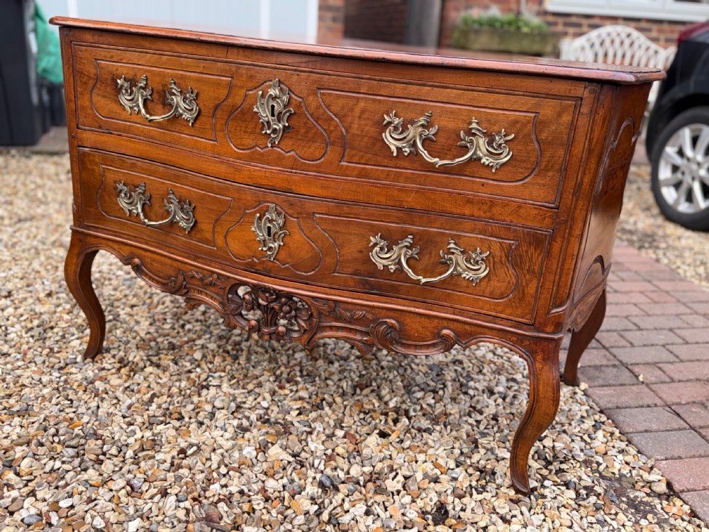 An 18th-century French Provincial walnut commode featuring two wide drawers with ornate brass handles, panelled carvings, and cabriole legs. View X