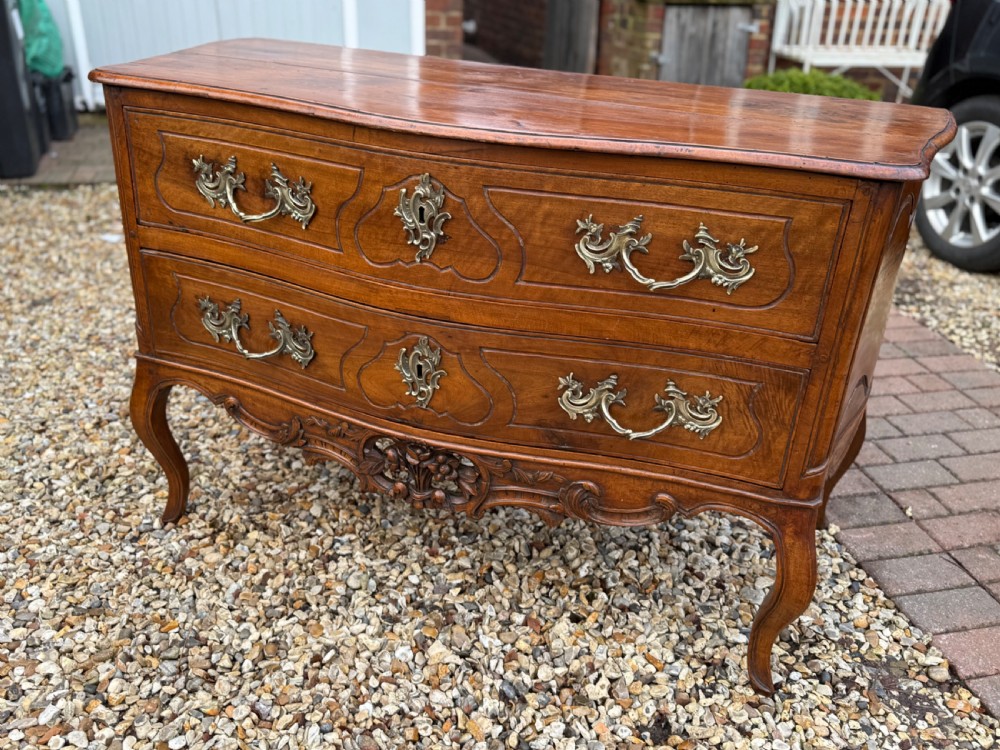 An 18th-century French Provincial walnut commode featuring two wide drawers with ornate brass handles, panelled carvings, and cabriole legs. View XI