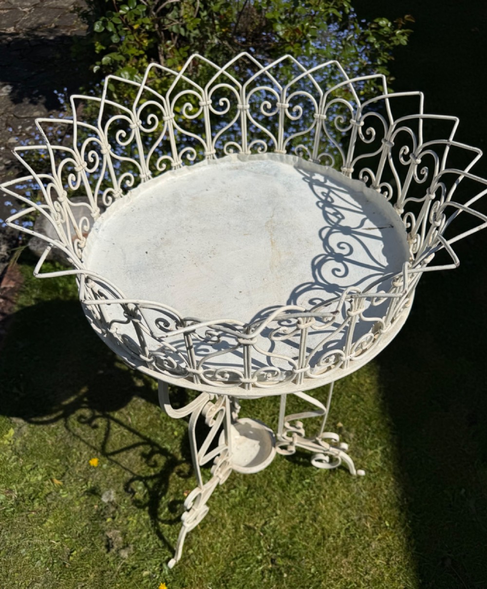 A nineteenth-century off-white painted wrought iron garden jardiniere featuring a tripod scrolled base and a lattice basket top. View V