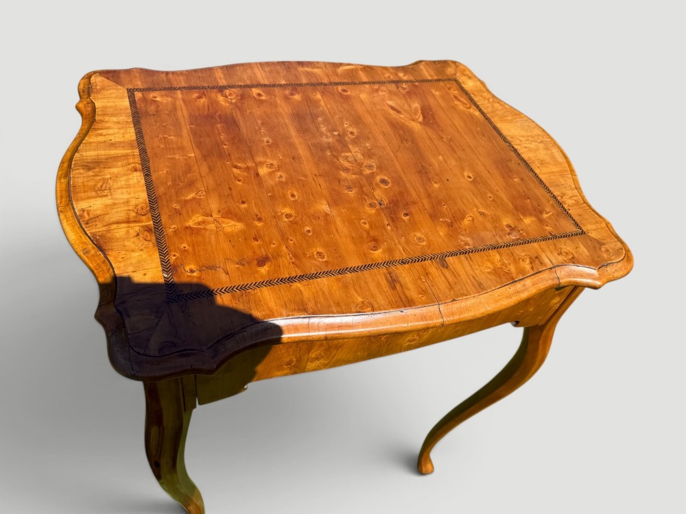 A golden-brown burr wood side table featuring a serpentine-edged top with inlay, a single drawer with a keyhole, and four slender cabriole legs. View II