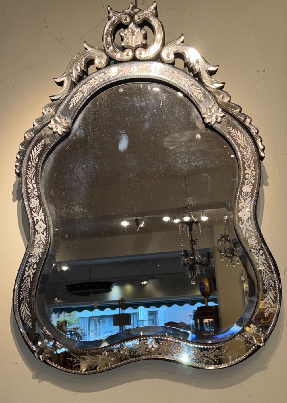 An ornate Venetian wall mirror featuring hand-etched floral glass borders, a decorative crest pediment, and a scalloped inner frame.