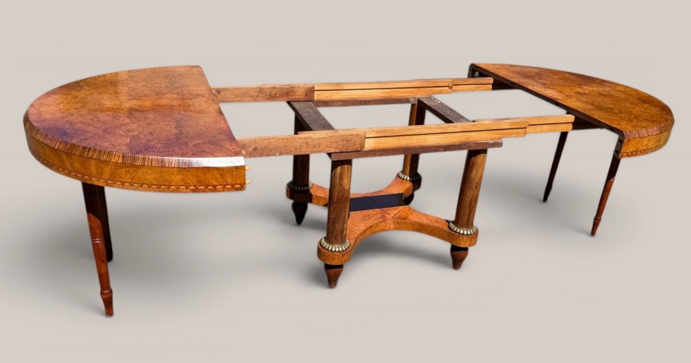 A circular Art Deco style extending dining table made of figured burr walnut veneer with a geometric inlaid apron and a quadruped base. View III
