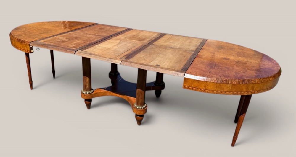 A circular Art Deco style extending dining table made of figured burr walnut veneer with a geometric inlaid apron and a quadruped base. View IV