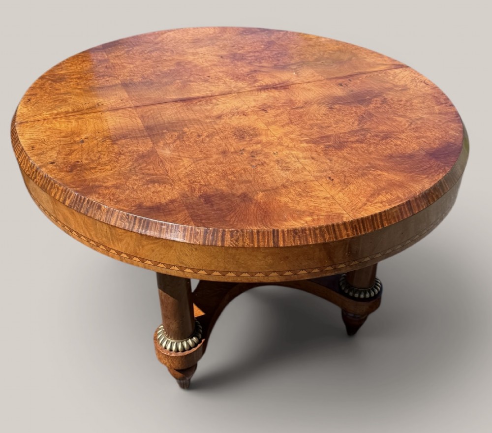 A circular Art Deco style extending dining table made of figured burr walnut veneer with a geometric inlaid apron and a quadruped base. View V
