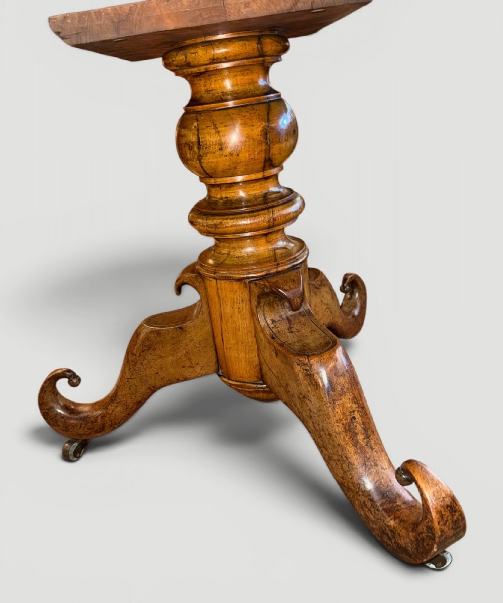 A circular antique gueridon table featuring a grey veined marble top, a figured walnut apron, a turned central pedestal, and scrolled tripod legs on castors. View II