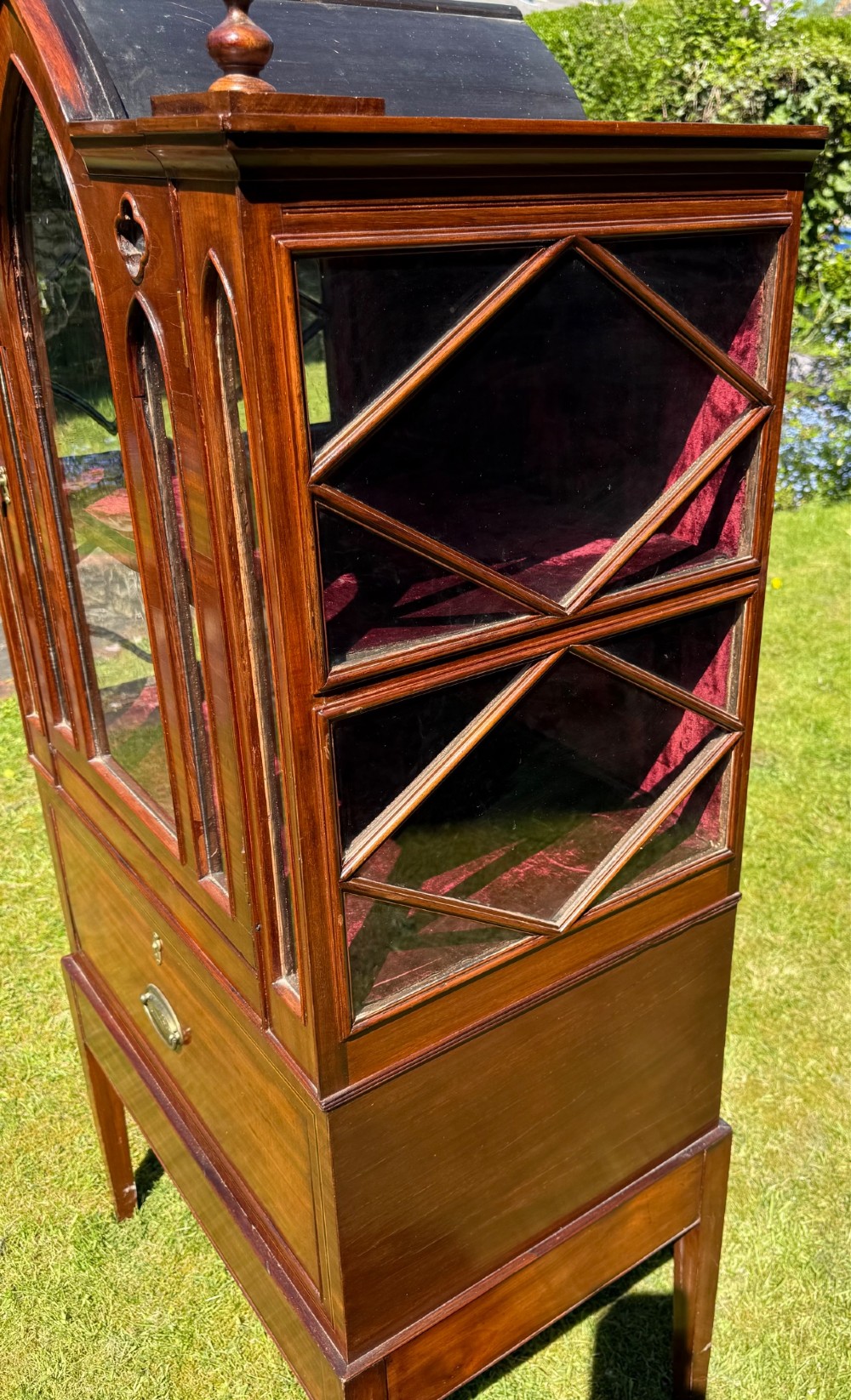 An antique mahogany Gothic Revival display cabinet on stand with pointed arch glass doors, side panels, and a lower drawer. View II