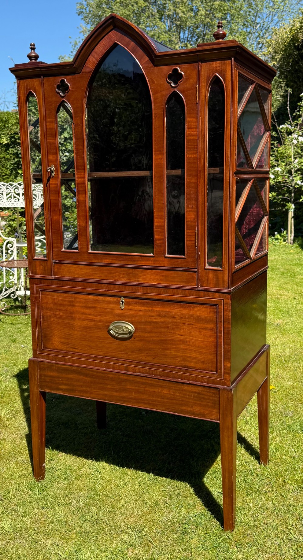 An antique mahogany Gothic Revival display cabinet on stand with pointed arch glass doors, side panels, and a lower drawer. View III