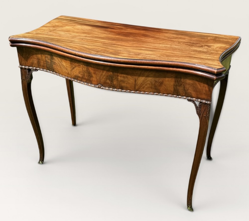 An antique warm brown mahogany card table with a serpentine front, carved cabriole legs, and a hinged fold-over top. View II