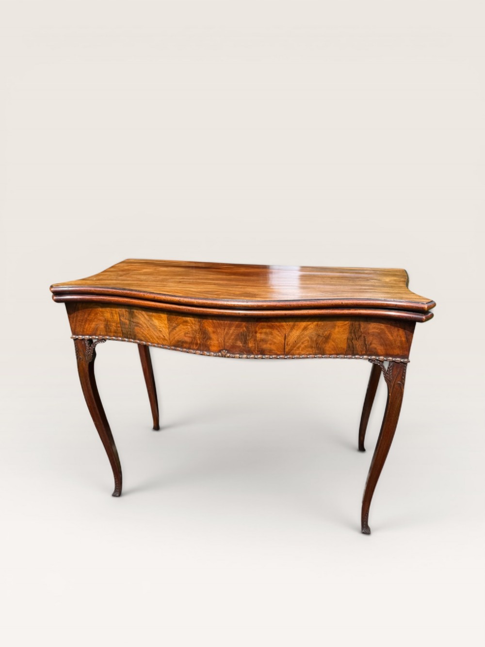 An antique warm brown mahogany card table with a serpentine front, carved cabriole legs, and a hinged fold-over top. View VIII