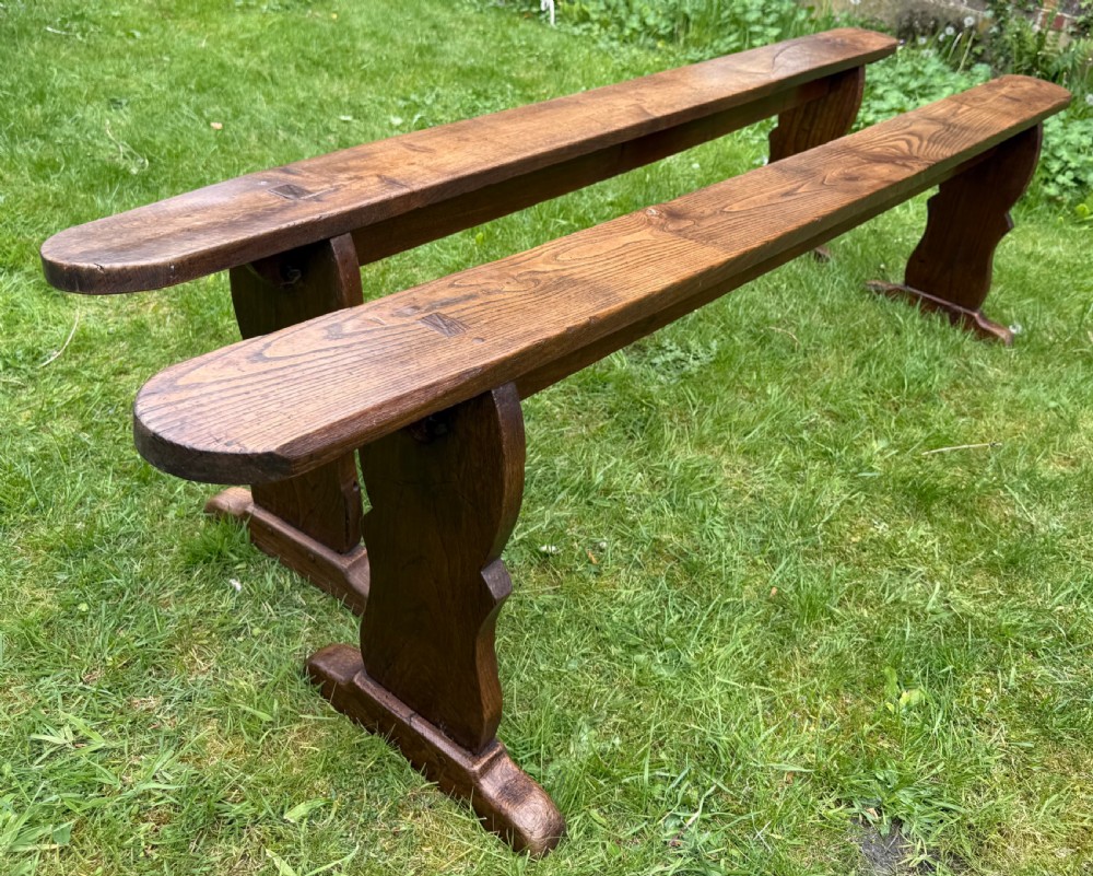 A pair of long French rustic oak benches with shaped trestle legs and smooth rounded seats showing distinct timber grain. View II