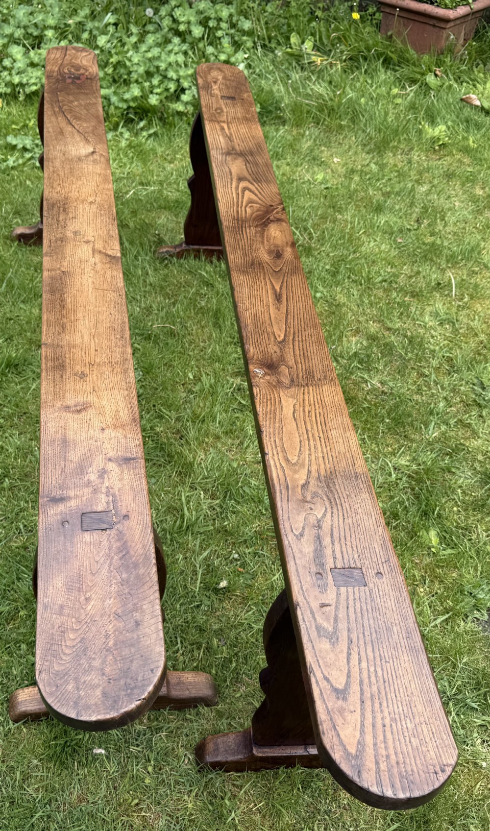 A pair of long French rustic oak benches with shaped trestle legs and smooth rounded seats showing distinct timber grain. View IV