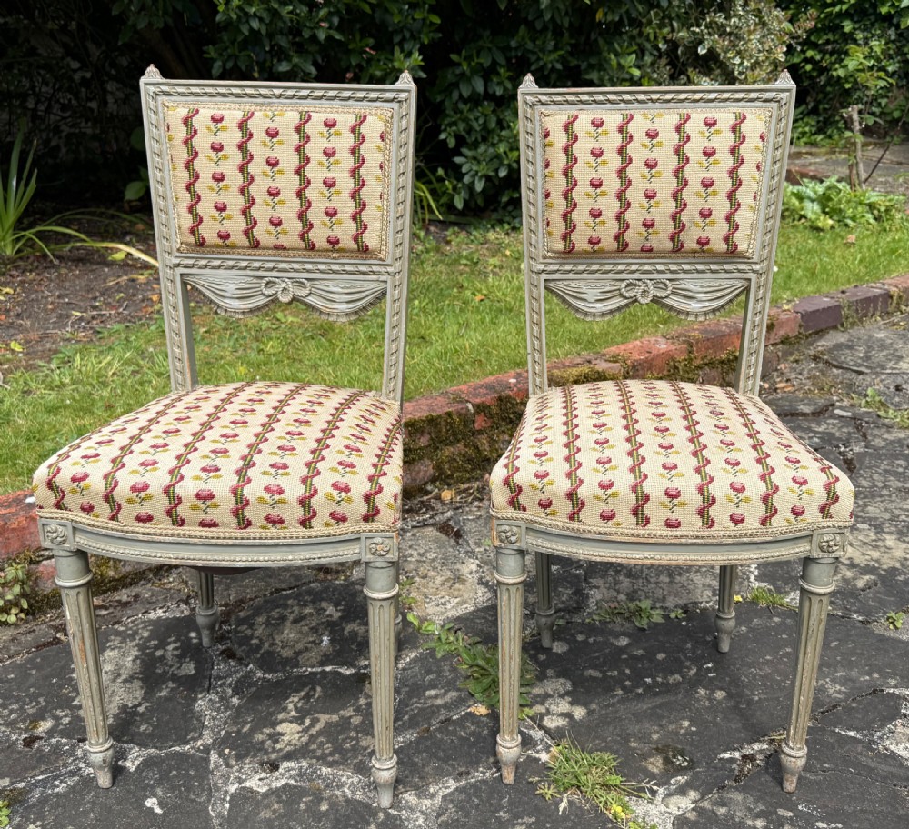 A pair of grey-painted Louis XVI style side chairs with fluted legs and floral needlepoint fabric upholstery.