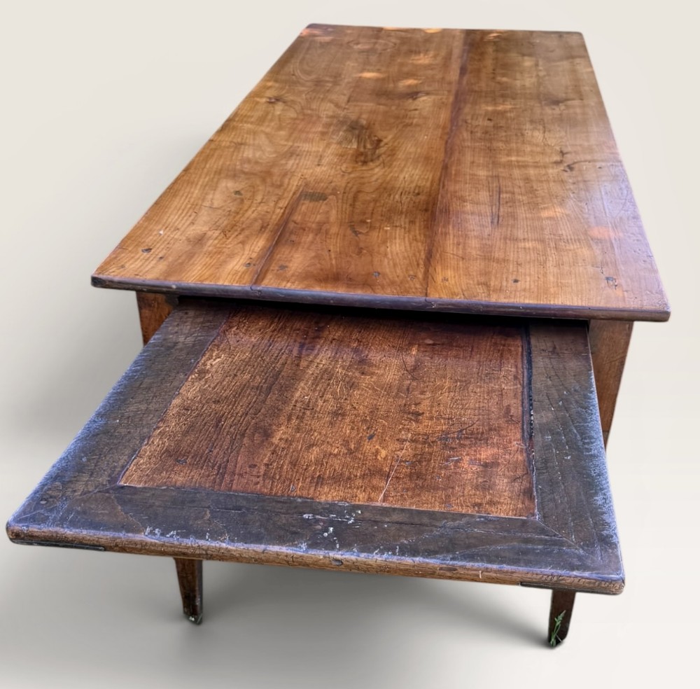 A rustic French farmhouse dining table featuring a rectangular plank top and an extended wooden bread slide at one end.