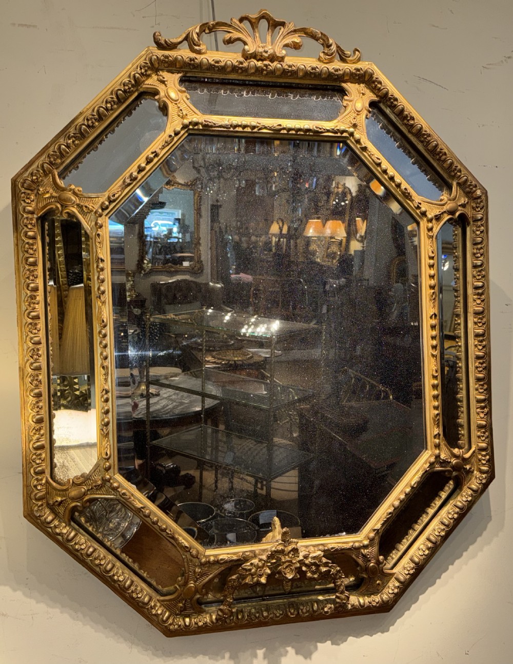 A 19th-century octagonal giltwood cushion wall mirror featuring ornate cresting, egg-and-dart moulding, and angled perimeter mirror plates.
