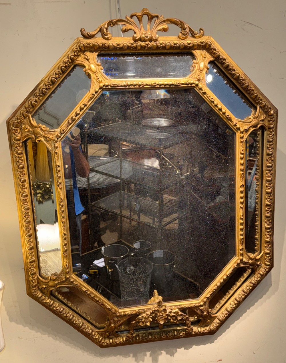 A 19th-century octagonal giltwood cushion wall mirror featuring ornate cresting, egg-and-dart moulding, and angled perimeter mirror plates. View III