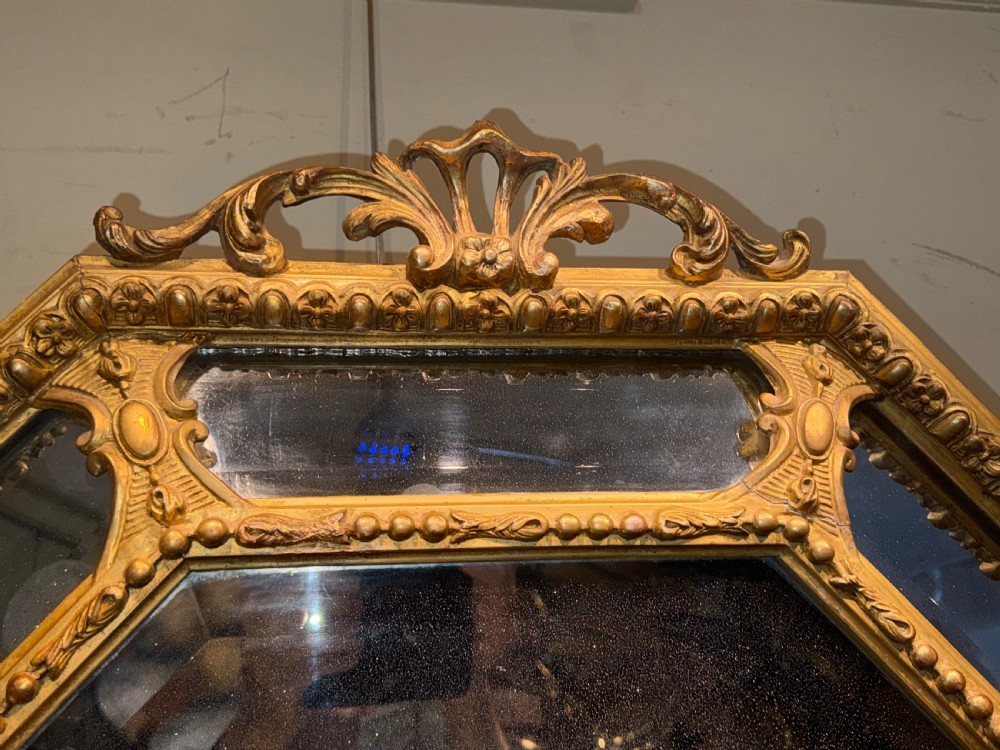 A 19th-century octagonal giltwood cushion wall mirror featuring ornate cresting, egg-and-dart moulding, and angled perimeter mirror plates. View V