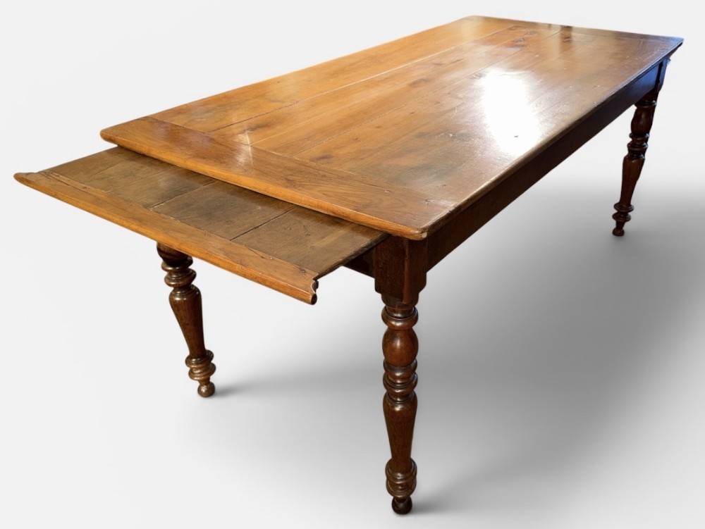 A warm brown wooden farmhouse dining table featuring turned legs, a plank top, and an extended slide-out side leaf.