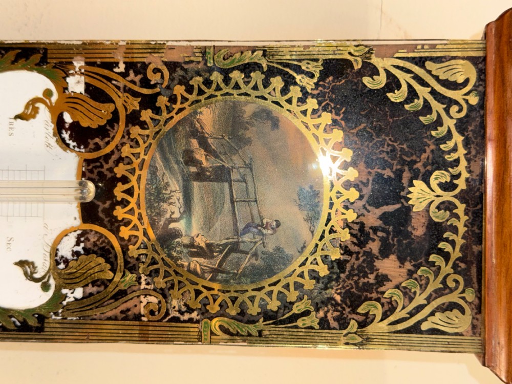 An antique wall-mounted stick barometer made from figured walnut featuring a central glass tube and decorative brass dial spandrels. View II