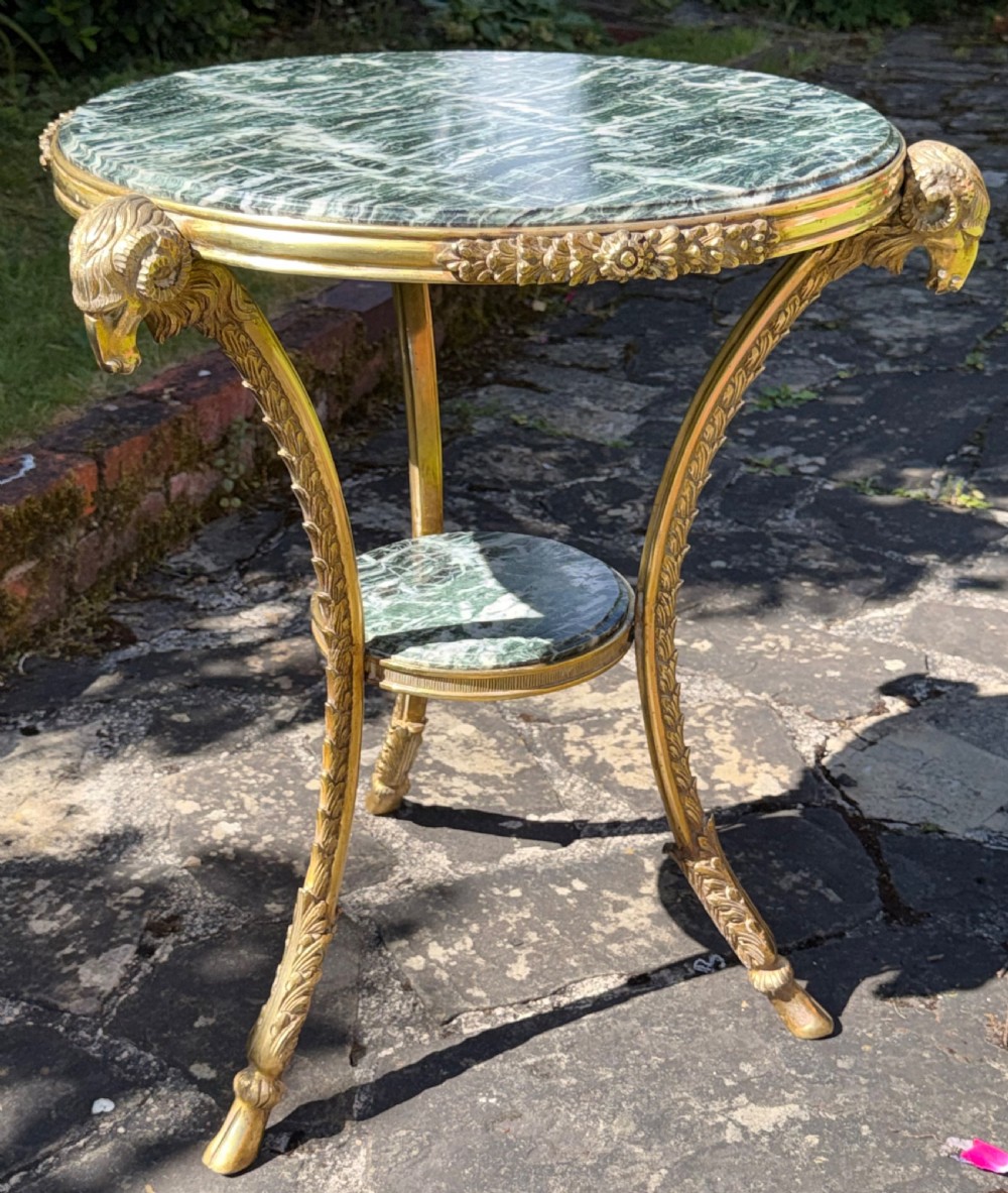 A Neoclassical style cast brass gueridon side table featuring a circular green marble top, a smaller tier below, and three legs styled with sculpted ram heads and hoof feet. View VIII