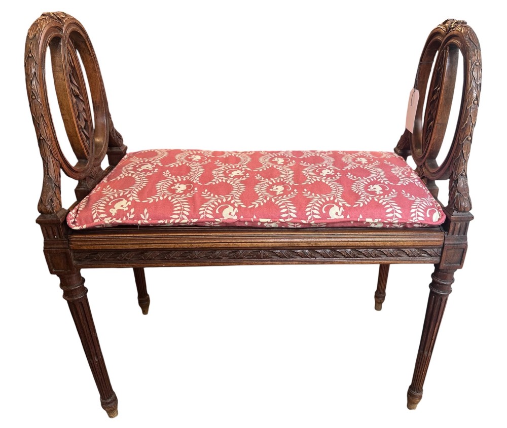 A late 19th-century French carved walnut window seat featuring raised oval ends, fluted tapered legs, and a pink patterned upholstered seat cushion.