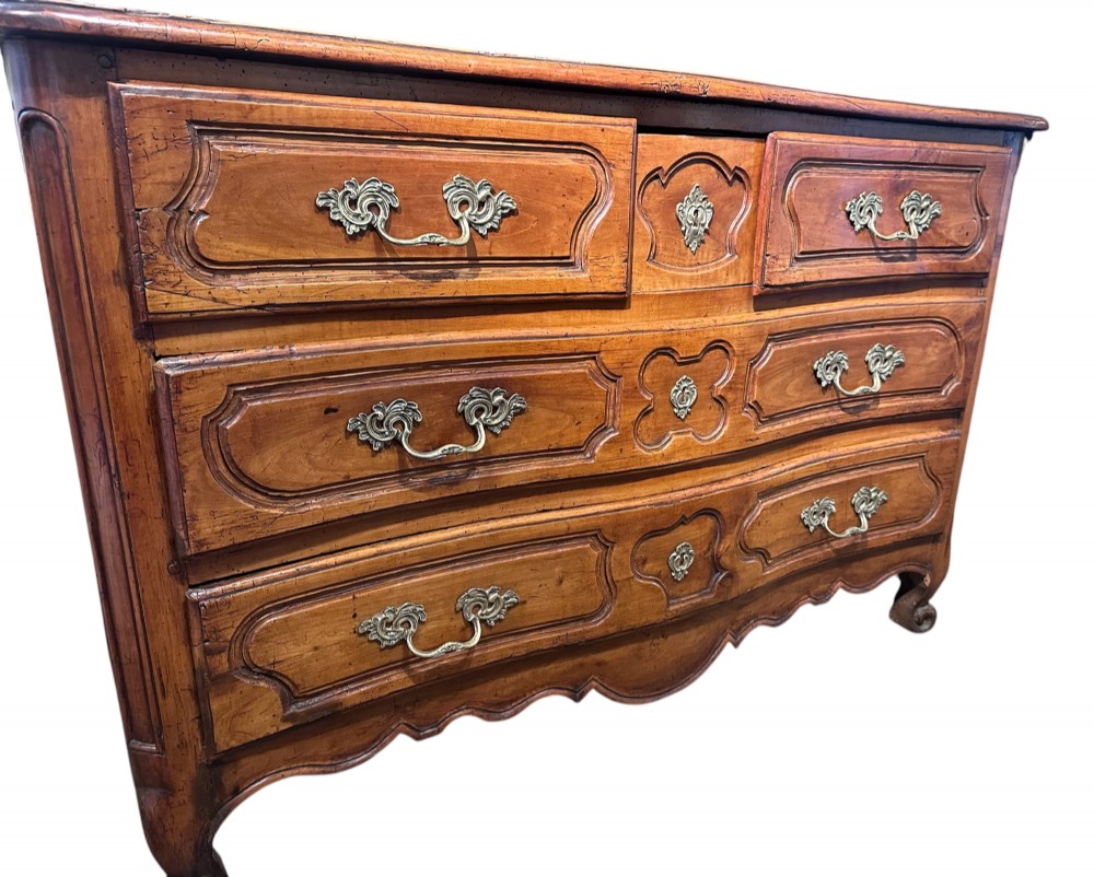 An 18th-century French Provincial cherry wood commode featuring three drawer tiers, ornate brass drop handles, moulded panel drawer fronts, and short cabriole feet.