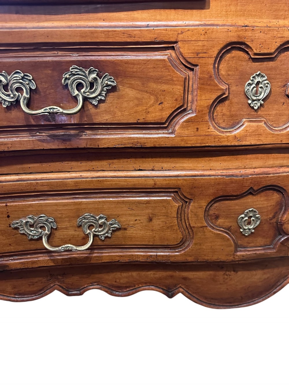An 18th-century French Provincial cherry wood commode featuring three drawer tiers, ornate brass drop handles, moulded panel drawer fronts, and short cabriole feet. View III