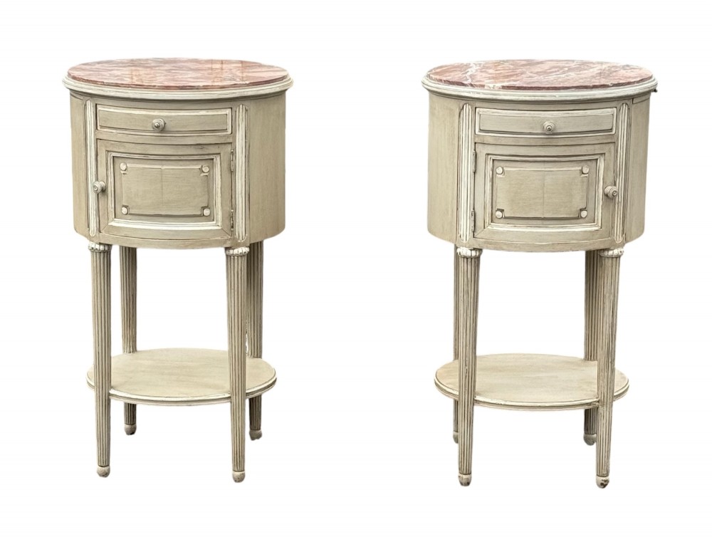 A pair of round 19th-century French painted bedside tables with pink marble tops, single drawers, cupboards, and fluted legs with a lower shelf.
