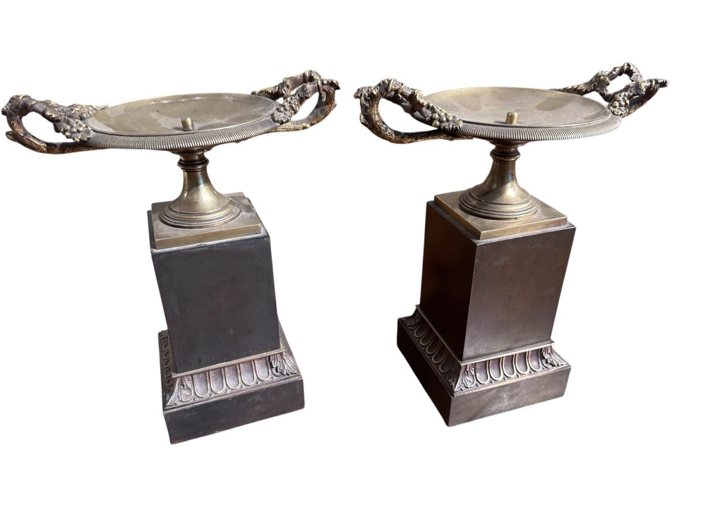 A pair of 19th-century French Empire style ormolu and bronze tazzas featuring grapevine handles and dark rectangular plinths.
