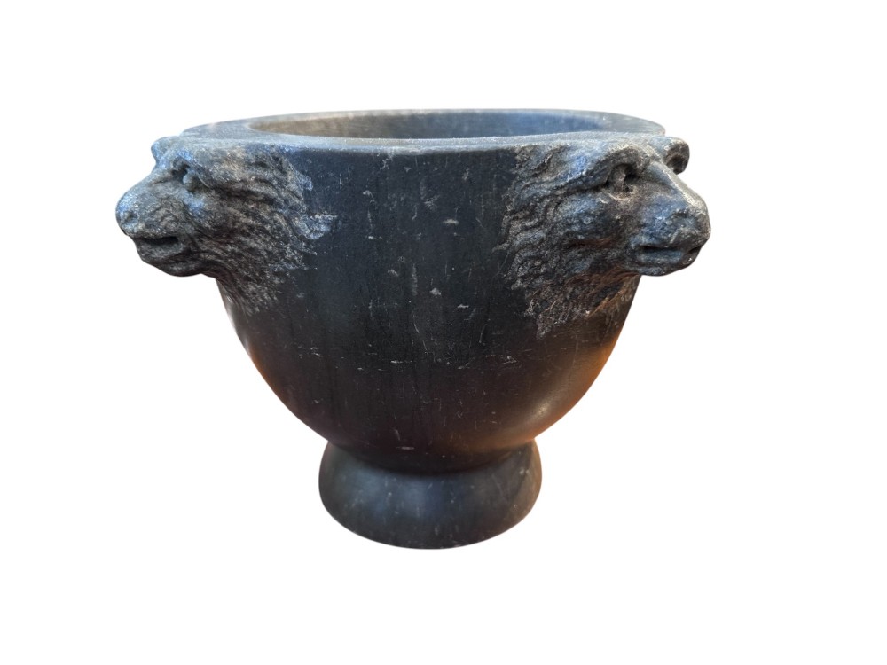An 18th century dark charcoal basalt stone mortar featuring carved lion head handles and a rounded pedestal foot.