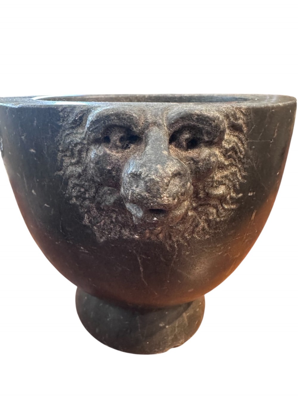 An 18th century dark charcoal basalt stone mortar featuring carved lion head handles and a rounded pedestal foot. View II