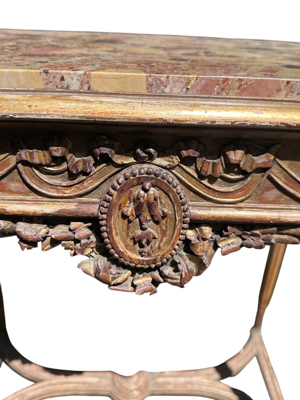 A 19th-century French giltwood side table featuring a variegated marble top, carved frieze with a central medallion, fluted tapered legs, and a curved stretcher with a central urn finial. View II