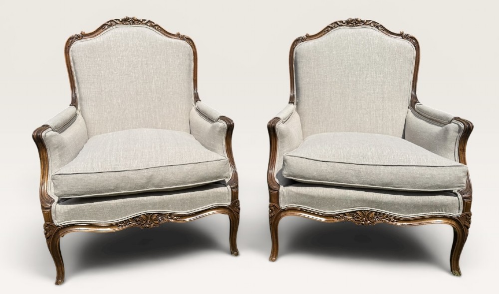 A pair of French Louis XV style Bergere armchairs featuring carved walnut wood frames and neutral light cream linen upholstery. View II