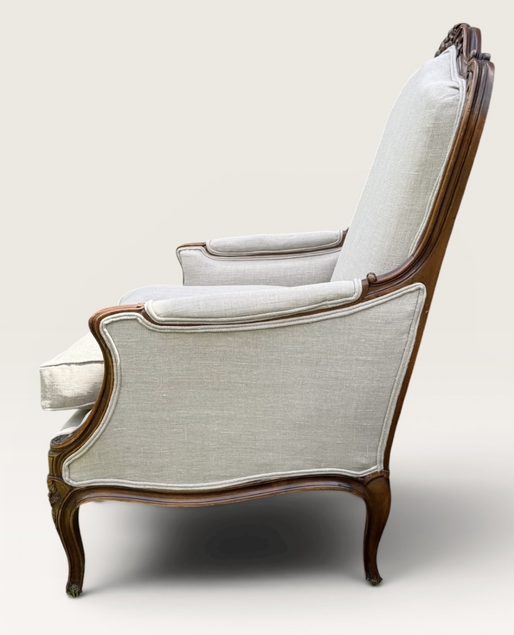 A pair of French Louis XV style Bergere armchairs featuring carved walnut wood frames and neutral light cream linen upholstery. View III