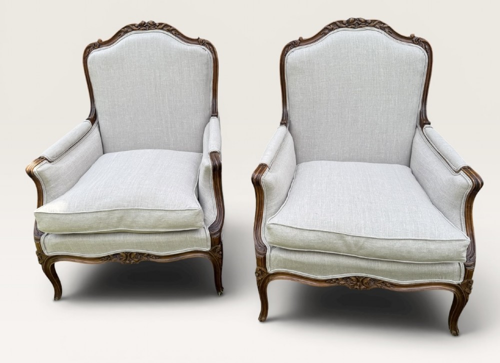 A pair of French Louis XV style Bergere armchairs featuring carved walnut wood frames and neutral light cream linen upholstery. View V