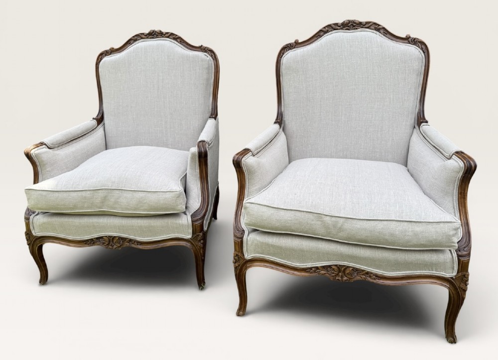 A pair of French Louis XV style Bergere armchairs featuring carved walnut wood frames and neutral light cream linen upholstery. View VI
