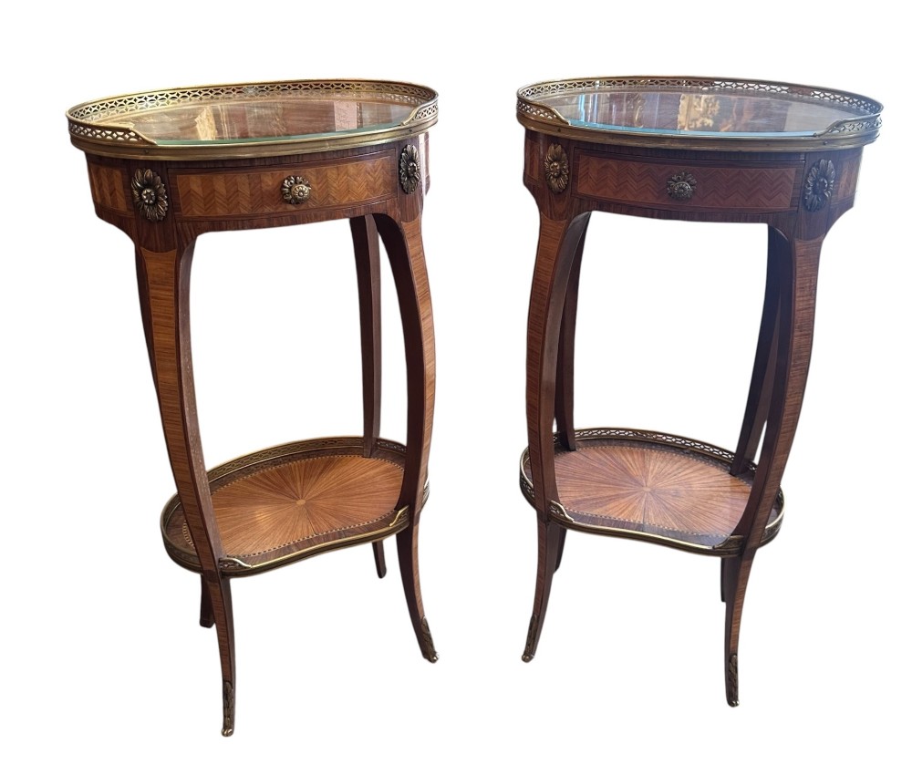 A pair of oval kingwood bedside tables featuring brass gallery rails, glass tops, lower undertier shelves, and slender cabriole legs with metal mounts.